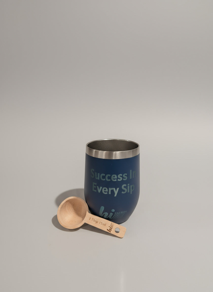 Blue tumbler with 'Success in Every Sip' text and wooden measuring spoon on a surface.
