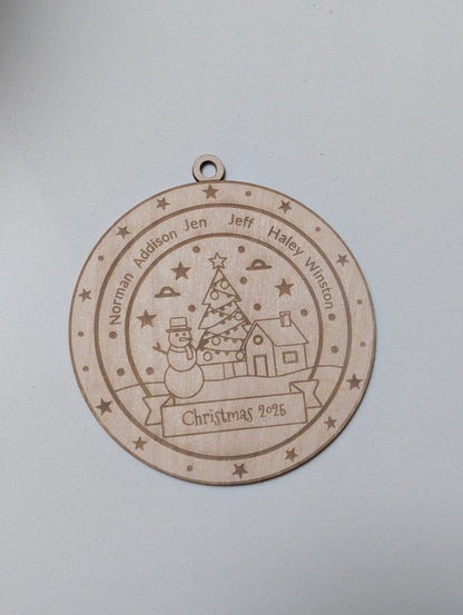 Wooden Christmas ornament with engraved design of a house, tree, and snowman on a light gray background.
